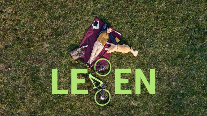 Mann liegt auf Wiese mit Hund und Mountainbike, Schriftzug Leben