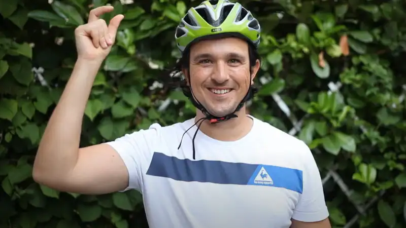 Ein American Express Mitarbeiter mit grünem Fahrradhelm vor einer grünen Hecke Ein American Express Mitarbeiter mit grünem Fahrradhelm vor einer grünen Hecke